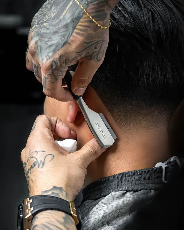 Manos de un barbero de Hermanos de Tijera afinando con navaja el contorno de un corte